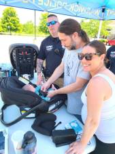 Town of Warwick Police Officer Nathaniel Petrosky, left, helps a young family with the installation of an infant car seat. Officers not pictured who participated: P.O. Sean McNamara, P.O. Andrew Cockburn, and P.O. Brian Siniscalchi.